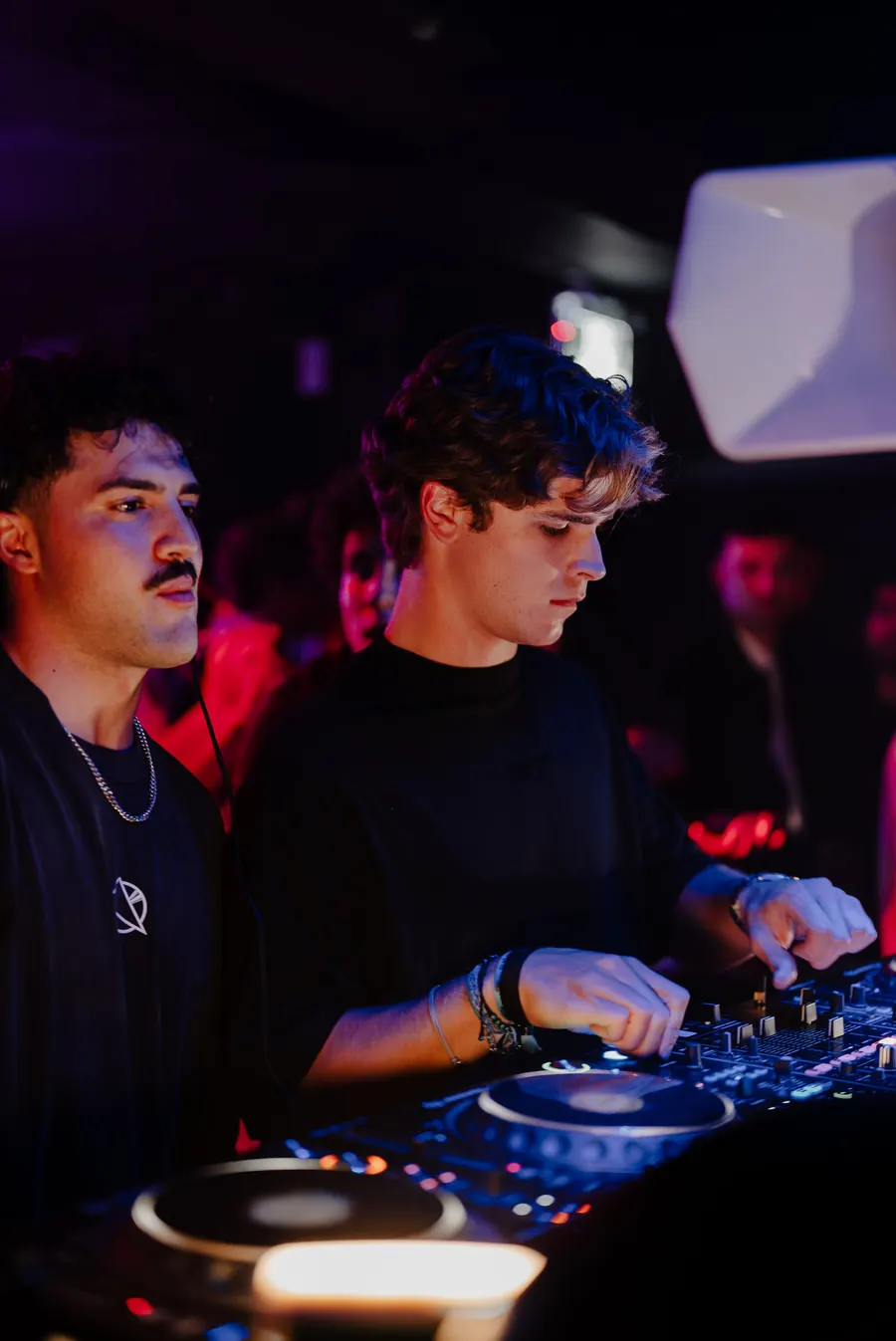Two DJs mixing on CDJs under red club lights