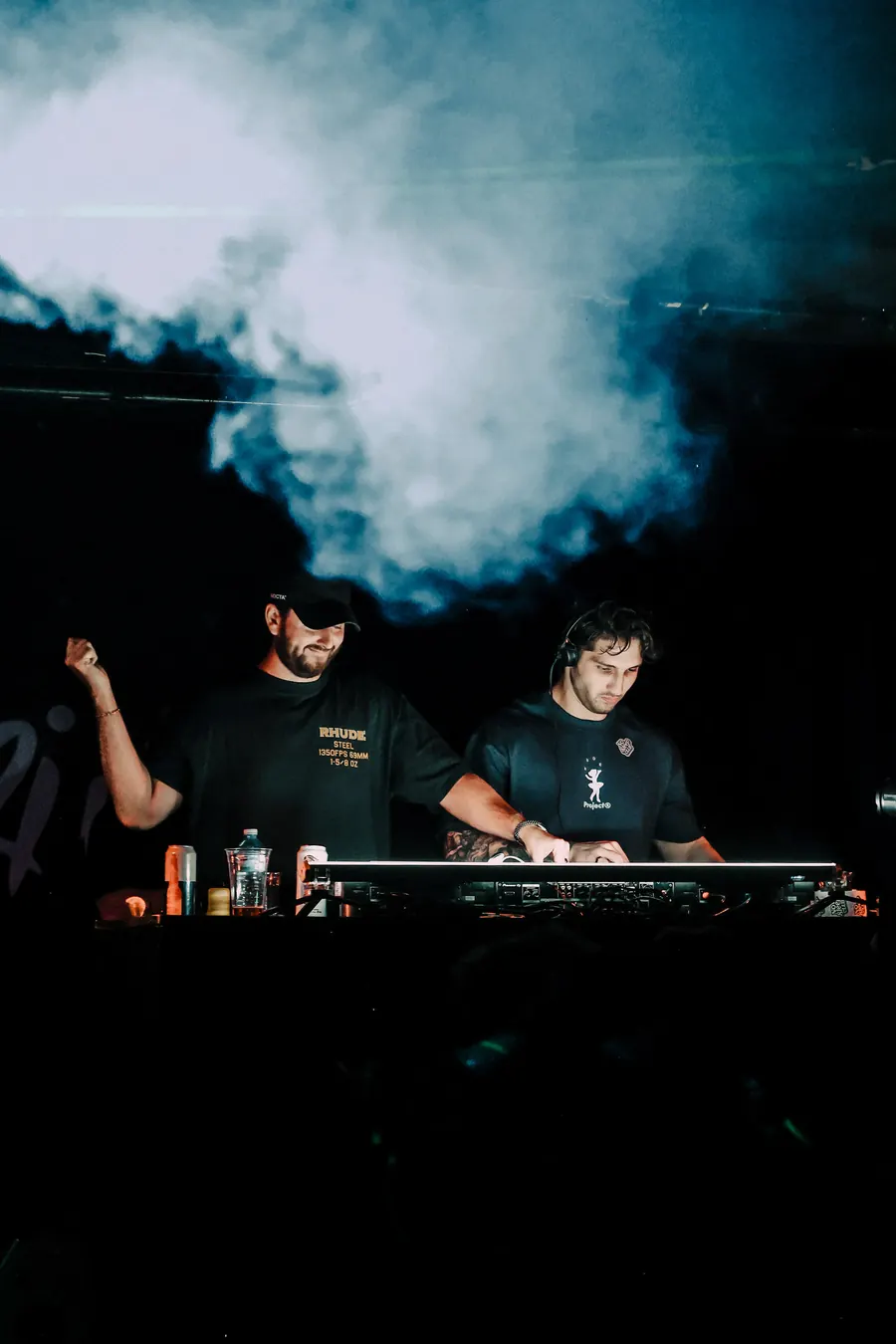 Two DJs behind the decks in haze and blue light